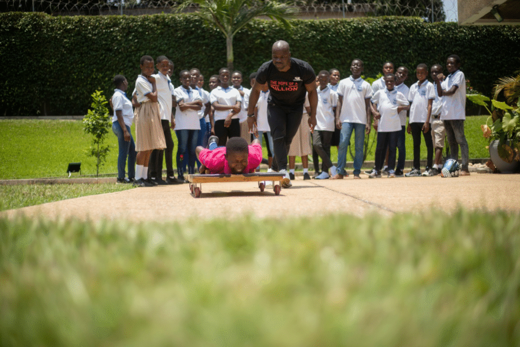 Akwasi Frimpong helps a child on a wooden skeleton with other children standing and watching in the background