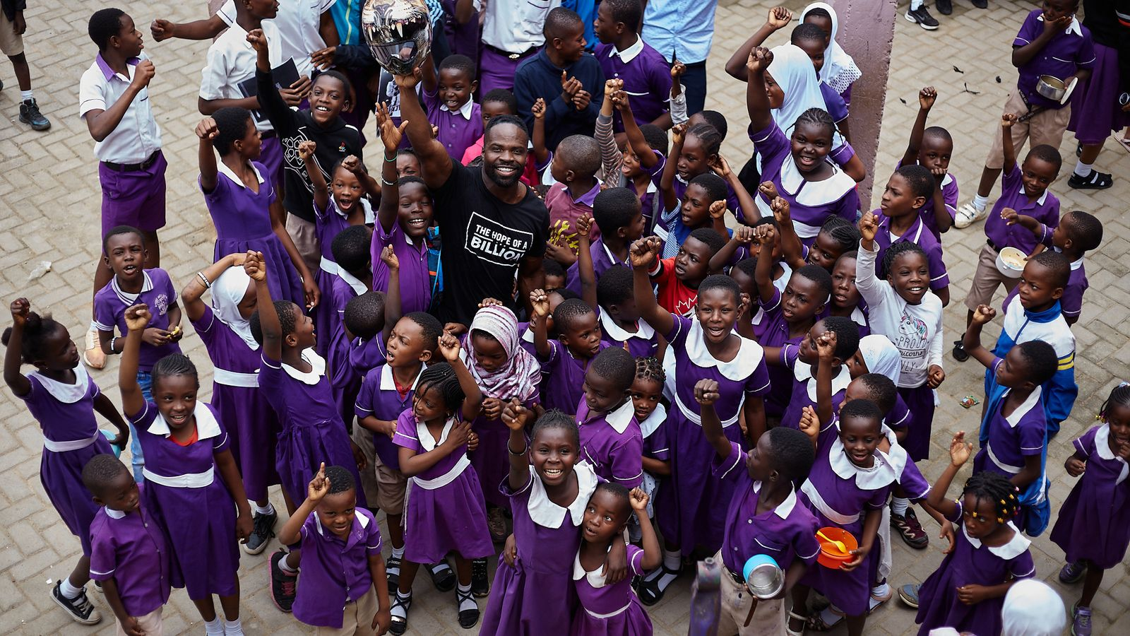 Akwasi Frimpong poses with a group of children, highlighting how education, sports, and mentorship provide essential opportunities for kids.