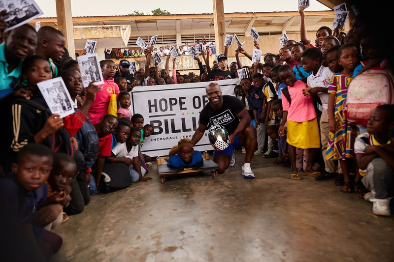 Akwasi Frimpong posing for a picture with kids with a Hope Of A Billion banner in the background